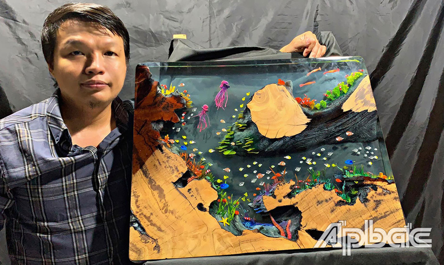 Nghệ nhân trẻ Đậu Viết Tùng bên mặt bàn với hình ảnh đại dương sống động vừa hoàn thành. 