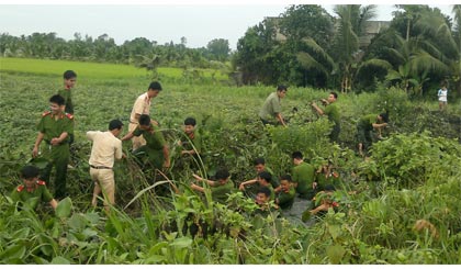 Dù trời mưa, các chiến sĩ công an vẫn lội kinh vớt lục bình. Ảnh: Thanh Bình