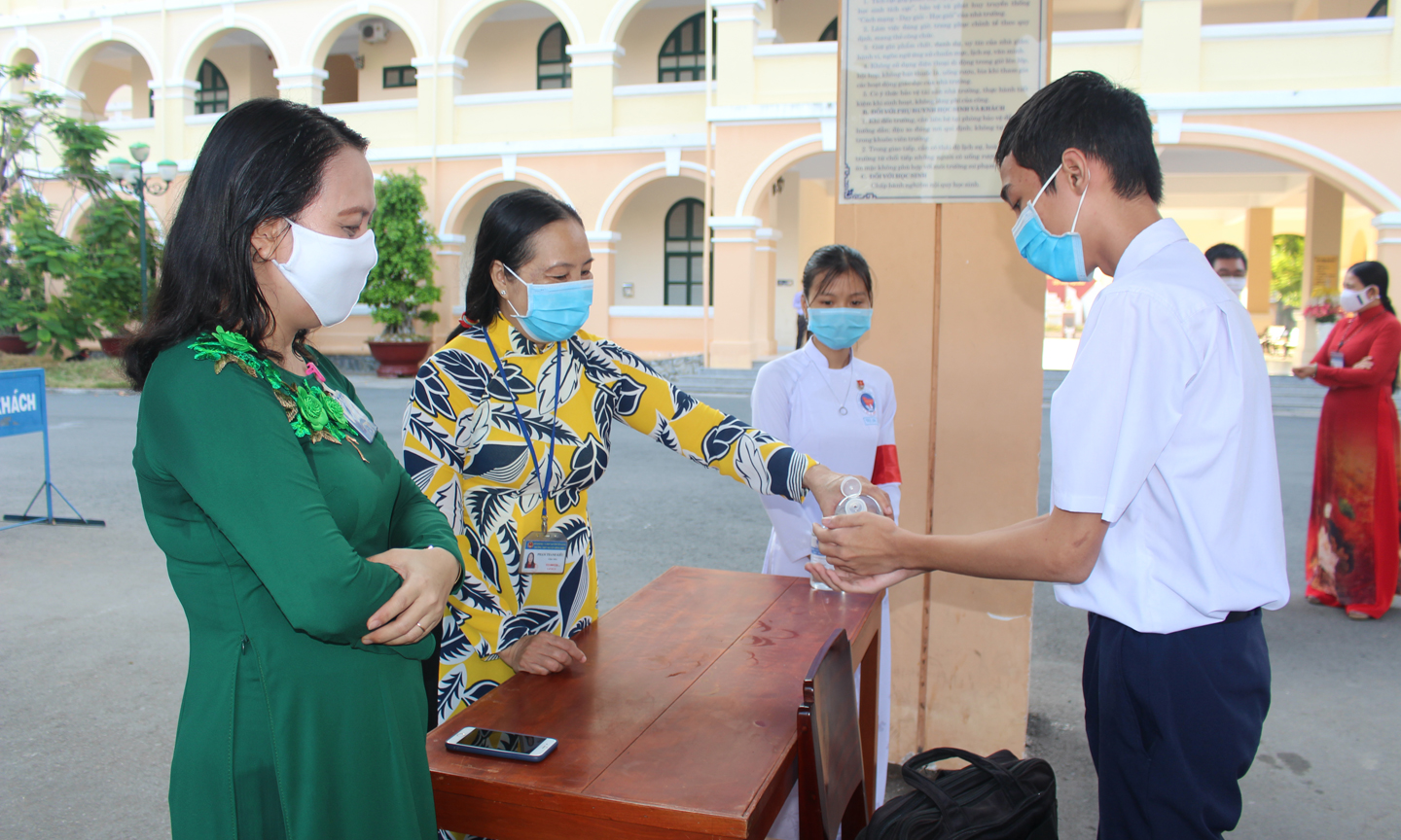 Ngay tại cổng trường Trường THPT Nguyễn Đình Chiểu, giáo viên trường đo thân nhiệt, sát khuẩn tay cho học sinh.