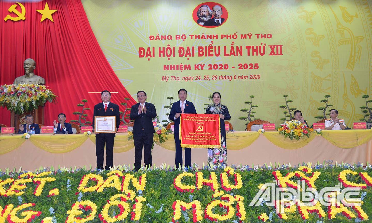 Đồng chí Võ Văn Bình trao bức trướng của Ban Chấp hành Đảng bộ tỉnh tặng Đảng bộ TP. Mỹ Tho với dòng chữ “Đảng bộ thành phố  Mỹ Tho đoàn kết, dân chủ, kỷ cương, năng động, đổi mới, phát triển”.                                                                                     Ảnh: Hạnh Nga