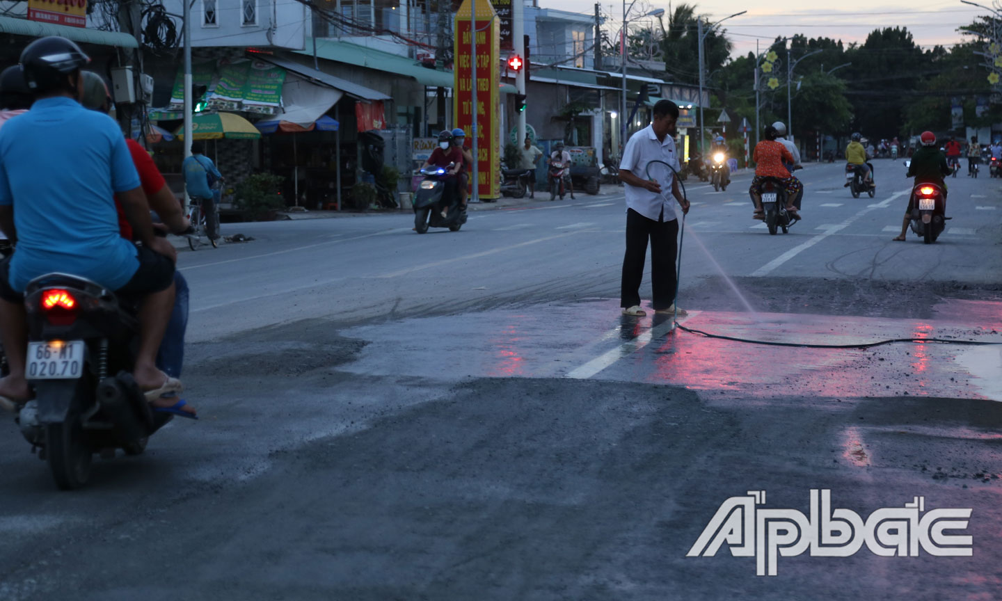 Người dân tưới nước cho đỡ bụi trên đoạn đường vừa được sửa chữa xong.