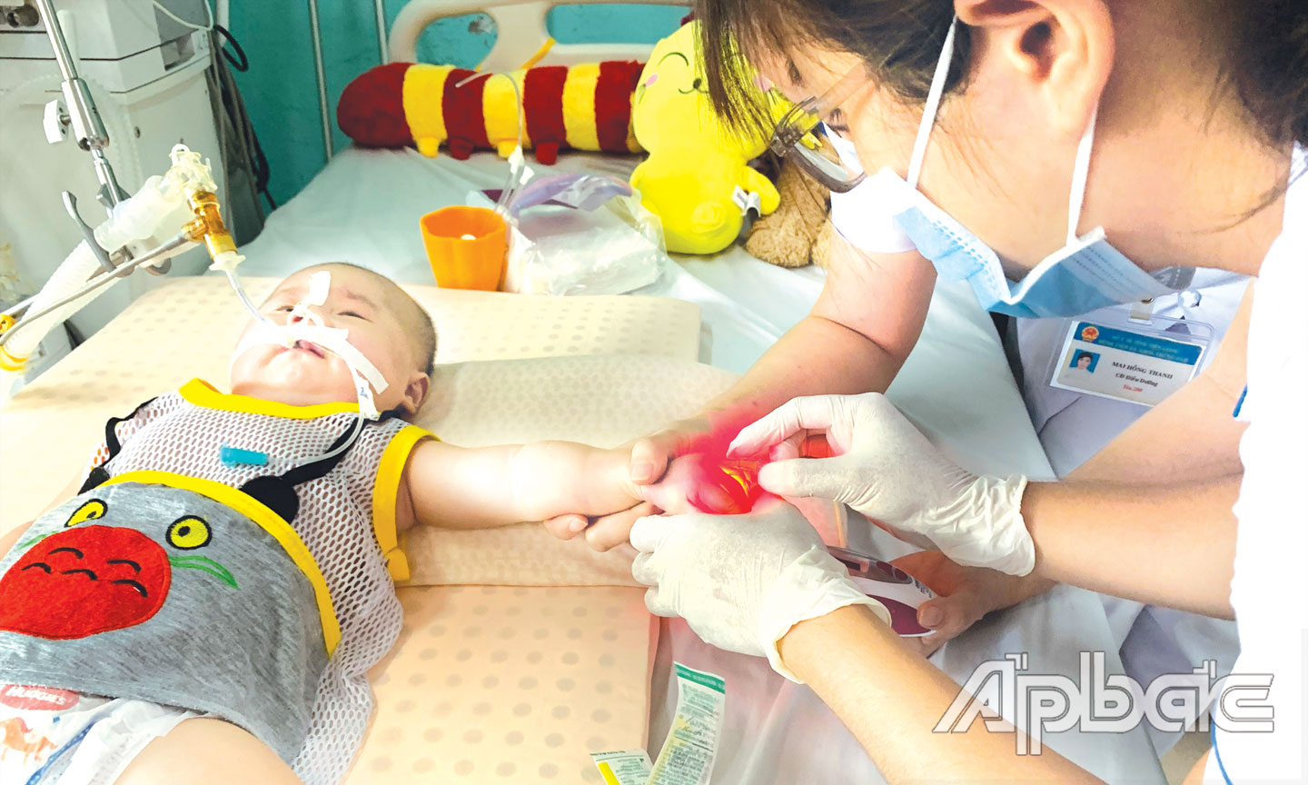 Các thầy thuốc phải soi đèn, nỗ lực tìm trên đôi tay bé tí những mạch máu gần như lặn mất của bé Đăng Khoa (8 tháng tuổi), con chị Đinh Thị Kim Chi, ngụ xã Hậu Mỹ Trinh, huyện Cái Bè, đang chống chọi với căn bệnh liệt tủy bẩm sinh.