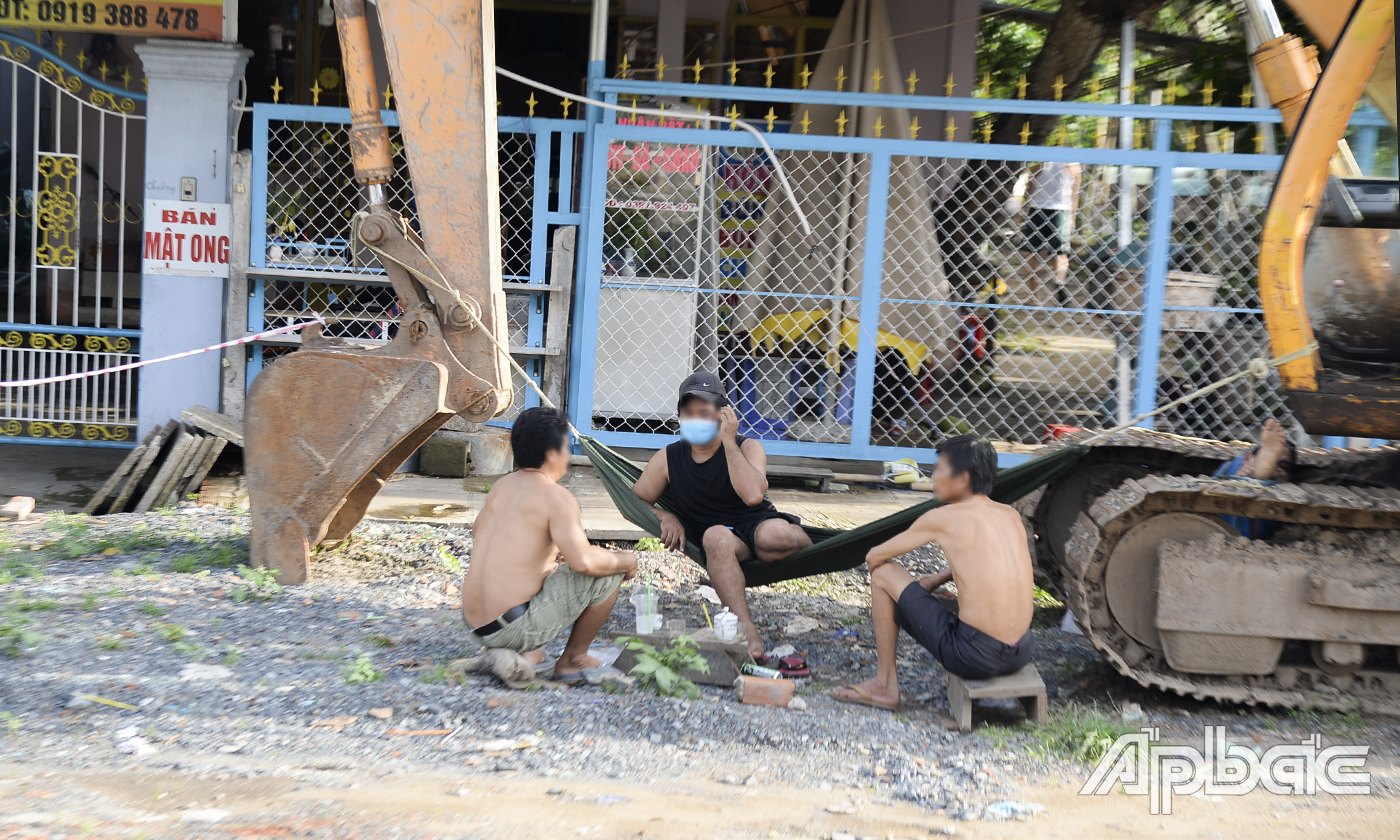3 người đàn ông tụ tập nói chuyện dưới chân cầu Nguyễn Trãi, thuộc phường 3, TP. Mỹ Tho, trong đó có 2 người không mang khẩu trang.
