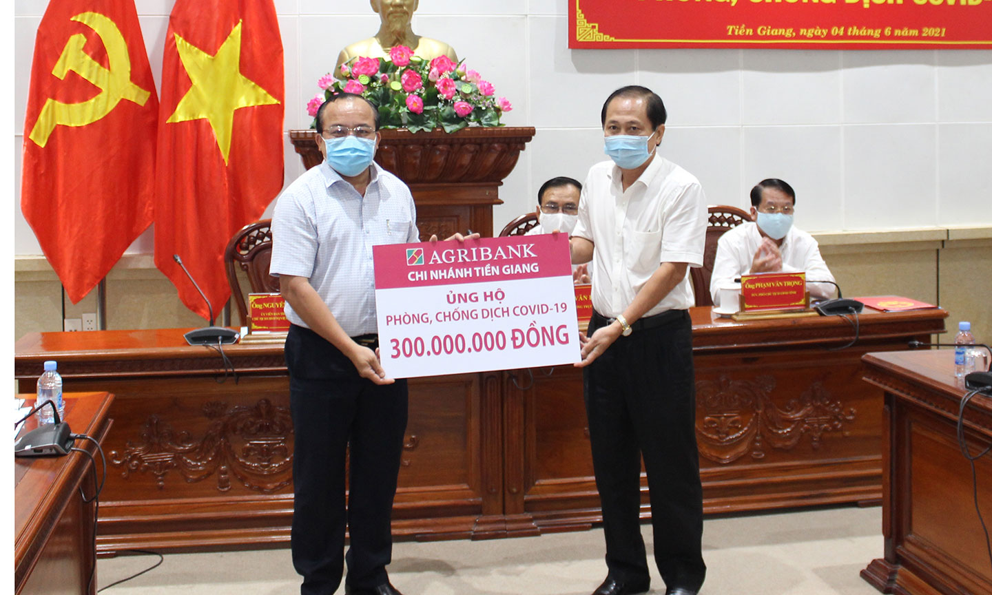 Giám đốc Agribank Tiền Giang Nguyễn Văn Huỳnh trao biển tượng trưng số tiền ủng hộ ủng hộ 300 triệu đồng vào sáng ngày 4-6-2021 tại Lễ Phát động đợt cao điểm quyên góp ủng hộ phòng, chống dịch covid 19 do Ủy ban Mặt trận Tổ quốc Việt Nam tỉnh Tiền Giang phát động.