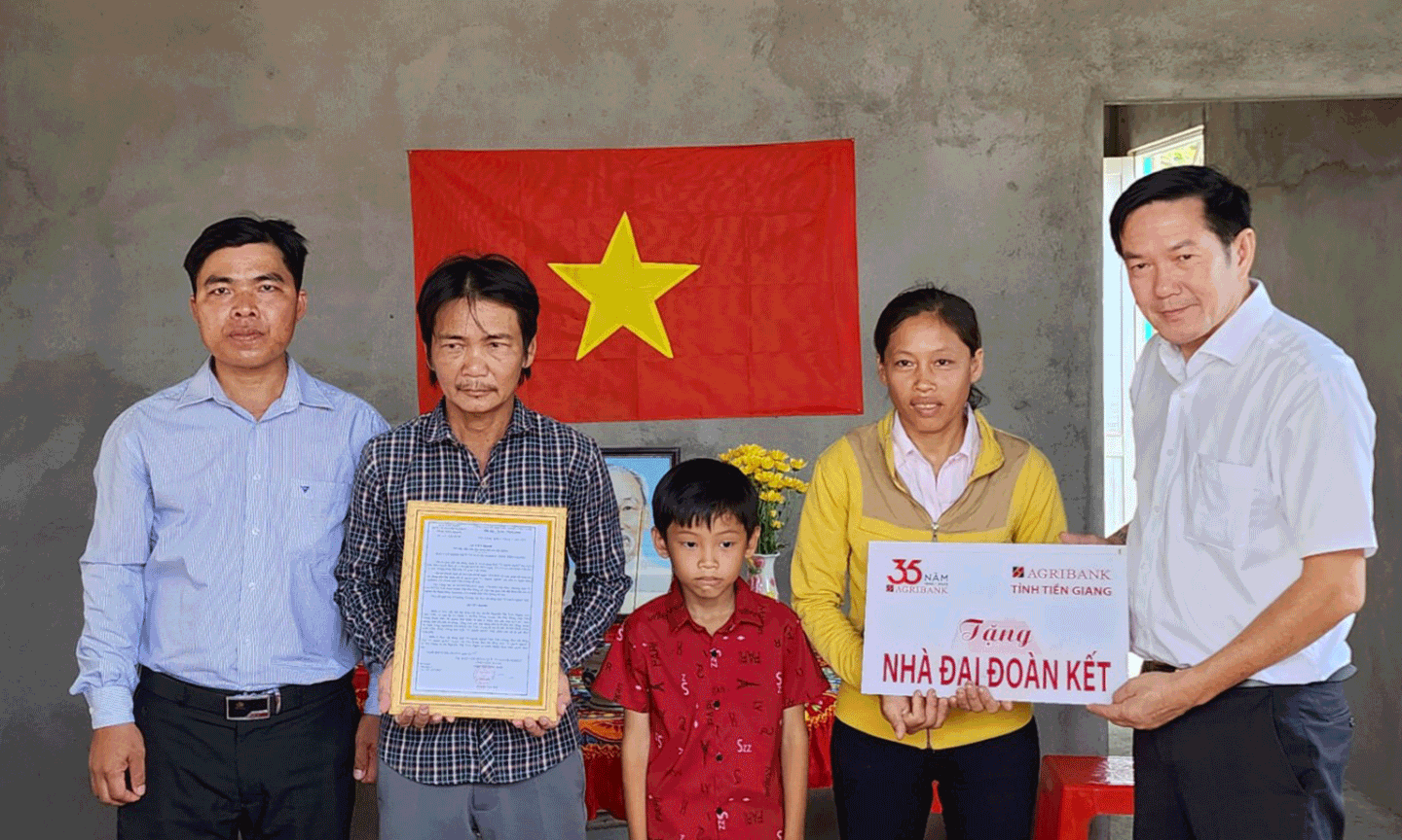 Ông Nguyễn Đắc Thắng, Huyện ủy viên, Phó Chủ tịch UBMTTQ huyện Tân Phú Đông (bìa trái) và Ông Trương Văn Đoàn, Phó Giám đốc Agribank Tiền Giang (bìa phải) trao quyết định bàn giao nhà và biển tượng trưng cho gia đình bà Nguyễn Thị Trúc Ngân.