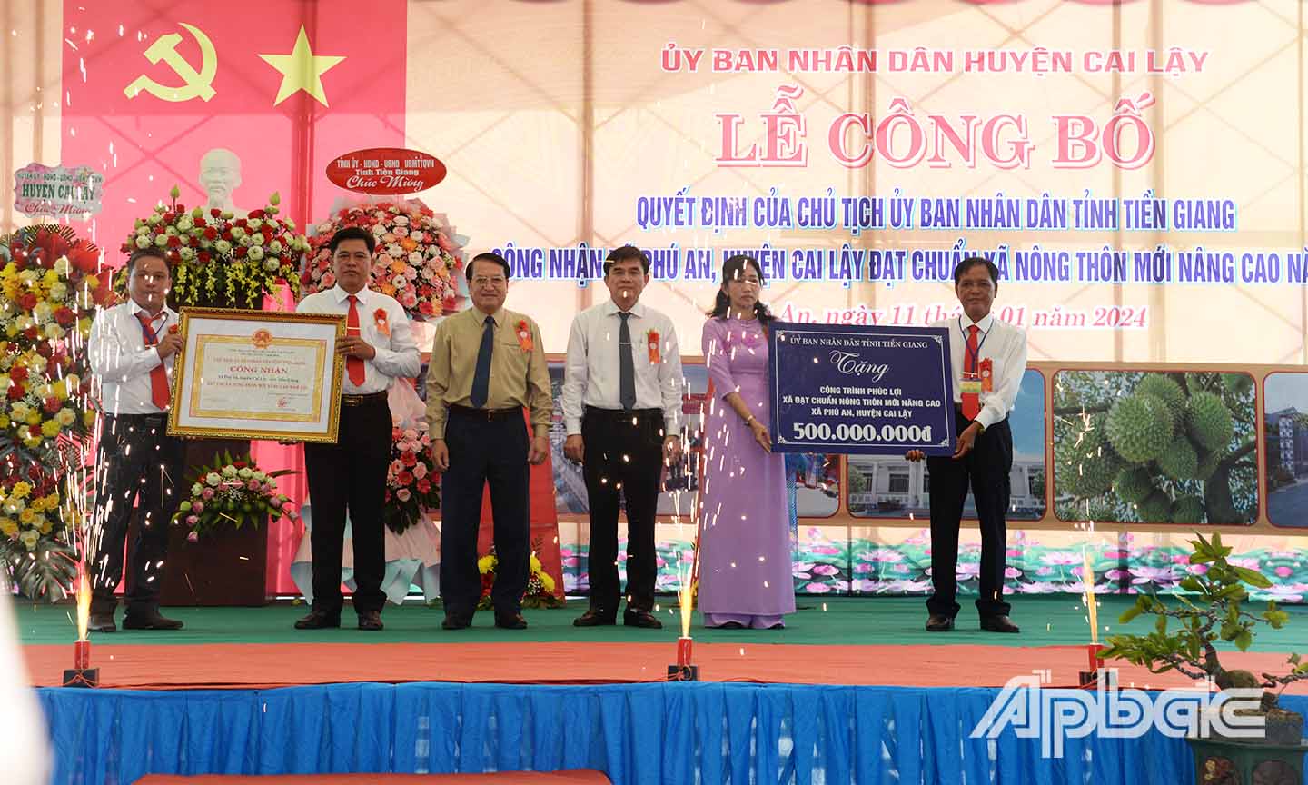 Đồng chí Nguyễn Văn Mười (thứ 3 từ phải sang) và đồng chí Phạm Văn Trọng (thứ 3 từ trái sang) trao bằng công nhận xã NTM nâng cao và bảng tượng trưng công trình phúc lợi trị giá 500 triệu đồng cho UBND xã Phú An.