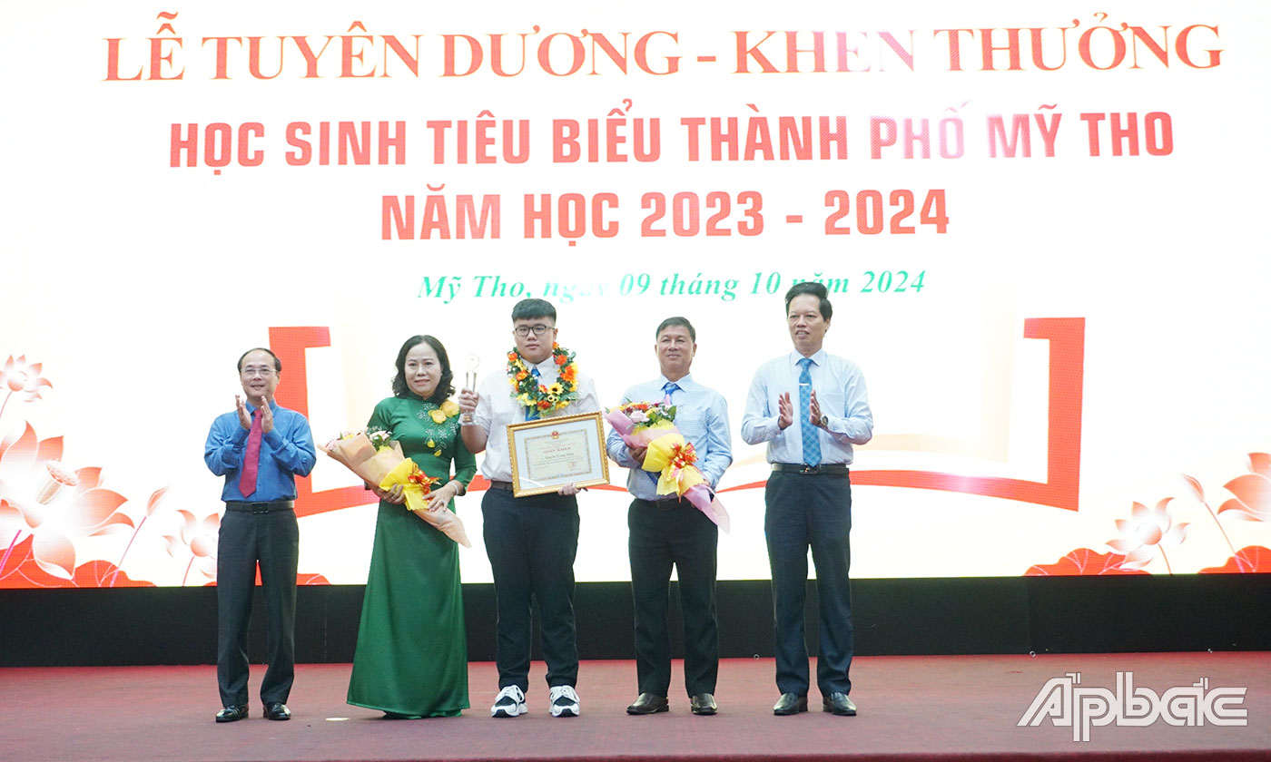 Đồng chí Nguyễn Thành Diệu, Phó Chủ tịch UBND tỉnh Tiền Giang và đồng chí Trần Kim Trát, Bí thư Thành uỷ Mỹ Tho trao Giấy khen và vòng nguyệt quế cho em học sinh tiêu biểu Nguyễn Trọng Nhân. 